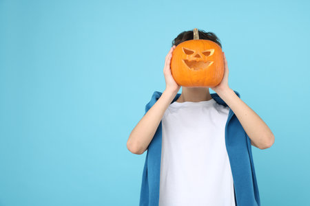 Halloween celebration. Boy holding pumpkin with carved face on light blue background, space for textの写真素材