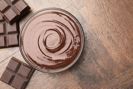 Bowl with melted chocolate and pieces on wooden table, flat lay. Space for textの写真素材