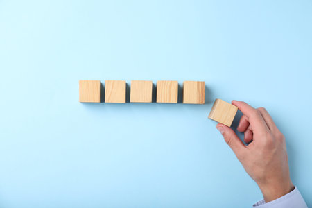 Man with wooden cubes on light blue background, top view