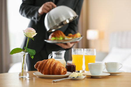 Waiter serving breakfast on wooden table in hotel room, closeupの写真素材
