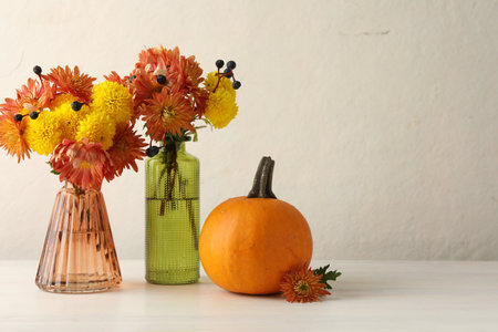 Autumn atmosphere. Vases with beautiful flowers, berries and pumpkin on white wooden table, space for textの写真素材