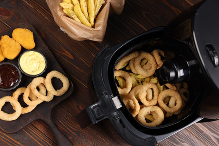 Air fryer with tasty squid rings, chicken nuggets, French fries and sauces on wooden table, flat layの写真素材
