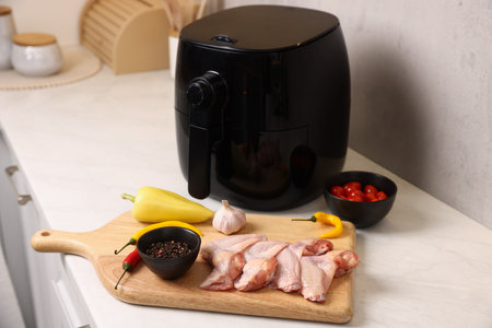 Air fryer, raw chicken thighs, tomatoes and spices on white marble countertop, closeupの写真素材