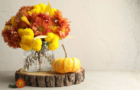 Autumn atmosphere. Vase with beautiful flowers and pumpkin on light gray table, space for textの写真素材