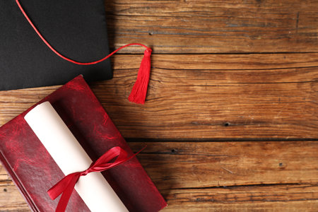 Graduation cap, book and diploma on wooden table, flat lay. Space for textの写真素材