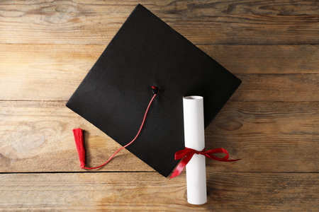 Graduation cap and diploma on wooden table, flat layの写真素材