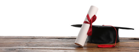 Graduation cap and diploma on wooden table against white background, space for textの写真素材