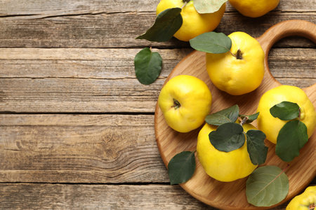 Fresh ripe quinces with leaves on wooden table, flat lay. Space for textの写真素材