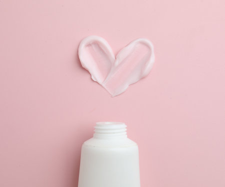 Heart shape made of moisturizing cream and tube on pink background, top viewの写真素材