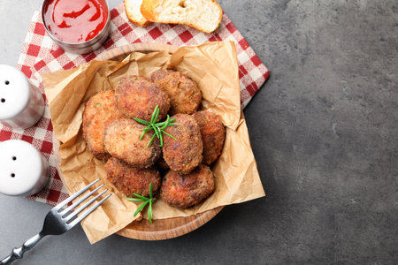 Delicious patties with rosemary in bowl, bread and ketchup served on gray textured table, flat lay. Space for textの写真素材
