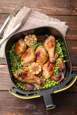 Air fryer basket with grilled chicken drumsticks, spices, green peas and tongs on wooden table, top viewの写真素材