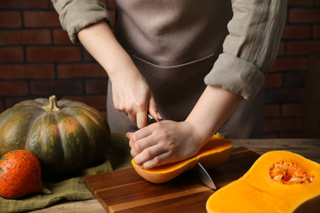 Woman cutting pumpkin at wooden table against brick wall, closeupの写真素材