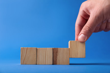 Man with wooden cubes on blue background, closeup. Space for textの写真素材