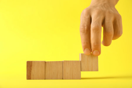Man with wooden cubes on yellow background, closeup. Space for textの写真素材