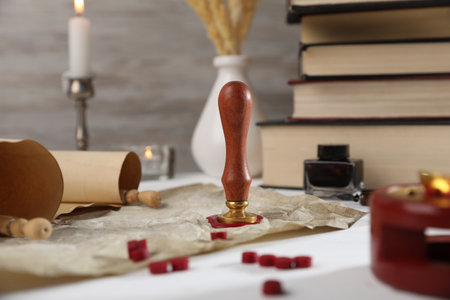 Scroll of old parchment paper, wax stamp, inkwell, books and burning candles on white wooden table, closeupの写真素材