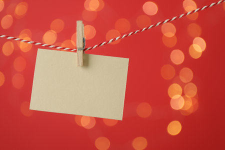 Blank card hanging on string against red background, bokeh effect. Mockup for designの写真素材