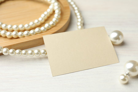 Blank card and pearl jewelry on white wooden table, closeup. Mockup for designの写真素材