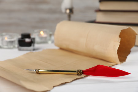 Scroll of old parchment paper, fountain pen, inkwell, books and burning candles on white wooden table, closeupの写真素材