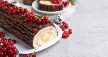 Delicious Yule log (traditional Christmas cake) with redcurrant on gray textured table, closeup. Space for textの写真素材