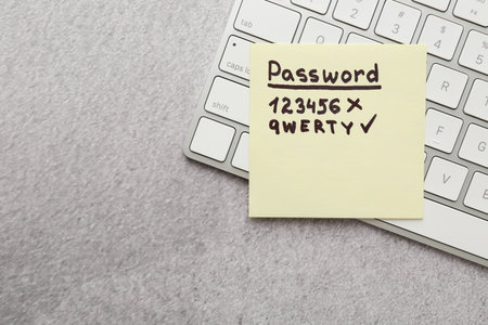Changing password. Sticky note with weak and strong passcodes near computer keyboard on gray table, top view. Space for textの写真素材