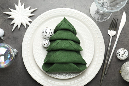 Festive table setting with Christmas tree made of napkin on gray background, flat lay