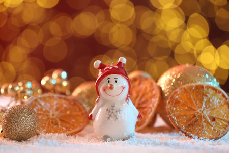 Cute decorative snowman, dried orange slices and golden baubles on artificial snow against blurred lights, closeupの写真素材