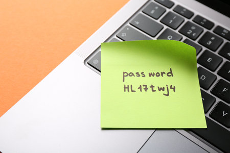 Paper note with password and laptop on orange background, closeupの写真素材