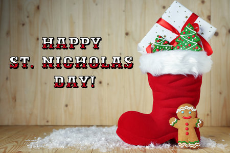 Happy St. Nicholas Day greeting card design. Red boot with gift box and gingerbread cookies on wooden backgroundの写真素材