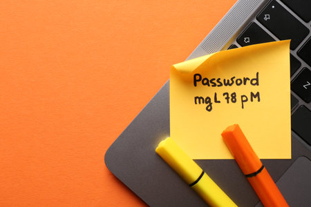 Paper note with password, markers and laptop on orange background, top view. Space for textの写真素材