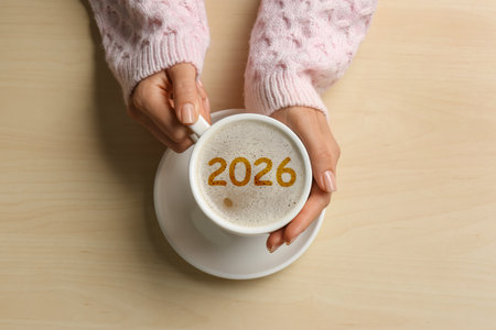 Woman holding cup of coffee with numbers on beige table, top viewの写真素材