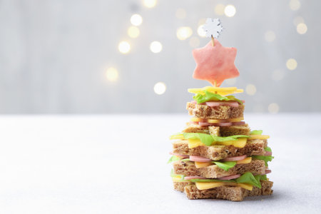 Christmas food. Fir tree made of bread, cheese, ham and lettuce on light gray table against background with blurred lights, space for text. Bokeh effectの写真素材