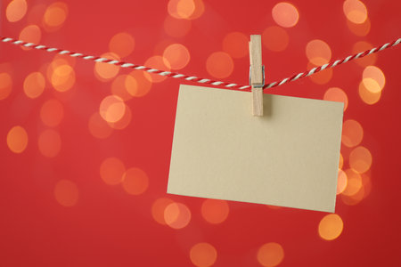 Blank card hanging on string against red background, bokeh effect. Mockup for designの写真素材