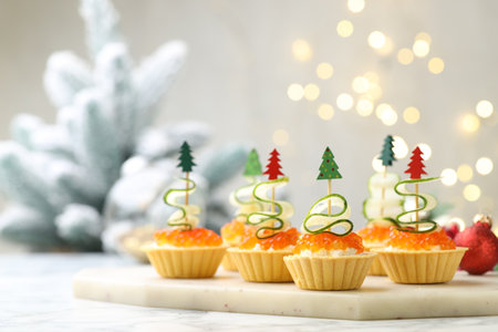 Christmas food. Tasty tartlets with red caviar, cream cheese, cucumber and decor on white marble table against background with blurred lights, closeup. Bokeh effectの写真素材