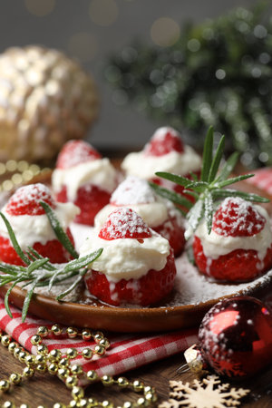 Christmas food. Santa hats made of strawberries, whipped cream, rosemary and decor on wooden table against background with blurred lights, closeup. Bokeh effectの写真素材