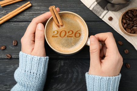 Woman holding cup of coffee with numbers on black wooden table, top view