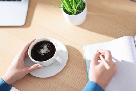 Woman with notebook and pencil having coffee break at wooden table, closeupの写真素材