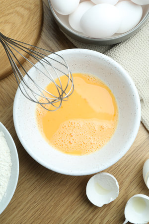 Beaten eggs in bowl on wooden table, flat layの写真素材