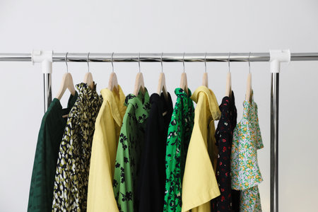 Different clothes hanging on rack against light background, closeupの写真素材