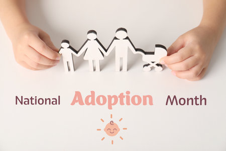 National Adoption Month poster with illustration of baby. Child holding wooden cutout of family on beige background, closeupの写真素材
