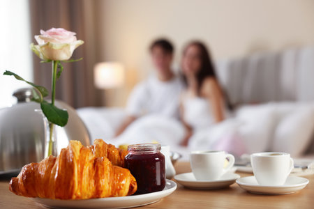 Delicious breakfast served on wooden table and couple staying in bed at hotel room, selective focusの写真素材