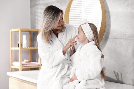 Happy mother and daughter in bathrobes at bathroomの写真素材