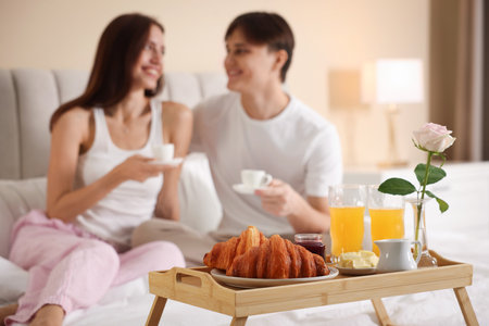 Tray with delicious breakfast and happy couple having coffee in bed, selective focus. Hotel room serviceの写真素材