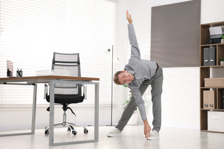 Young businessman doing stretching exercise in officeの写真素材
