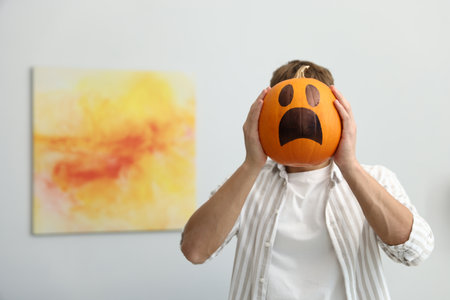 Halloween celebration. Man holding pumpkin with drawn spooky face at home, space for textの写真素材
