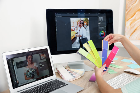 Professional retoucher with color palettes editing photo on computer and laptop at table in office, closeupの写真素材