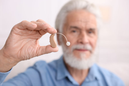 Senior man with hearing aid on light background, selective focus