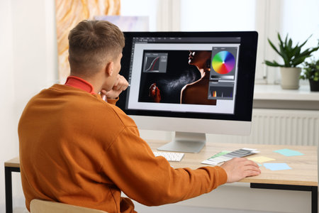 Professional retoucher editing photo on computer at table in office, back view