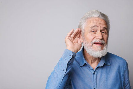 Senior man with hearing problem on light gray background.