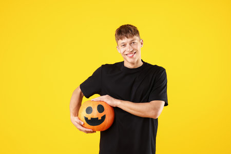Halloween celebration. Man holding pumpkin with drawn face on orange backgroundの写真素材