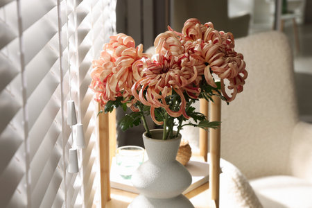 Beautiful pink chrysanthemum flowers in vase on wooden shelf indoorsの写真素材